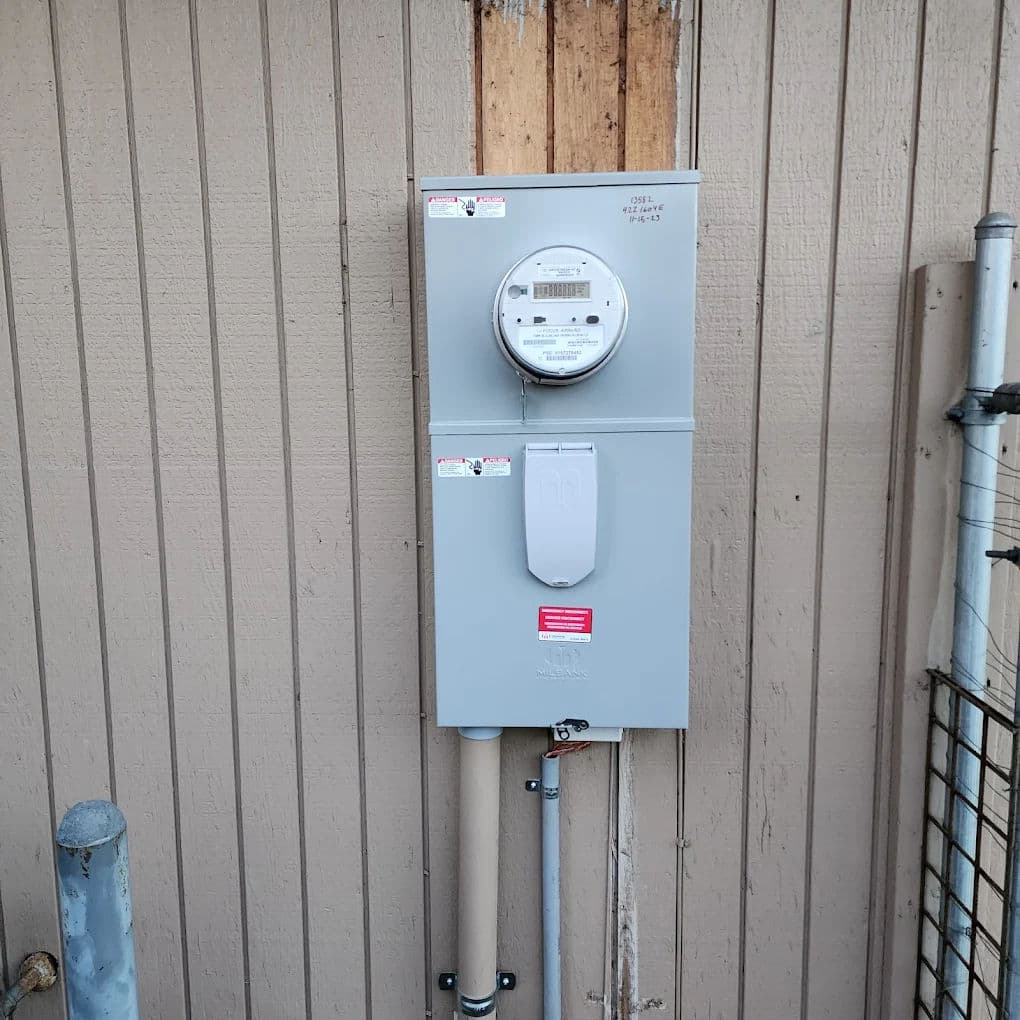 Electric meter mounted on a wooden wall, featuring a digital display and utility connections.
